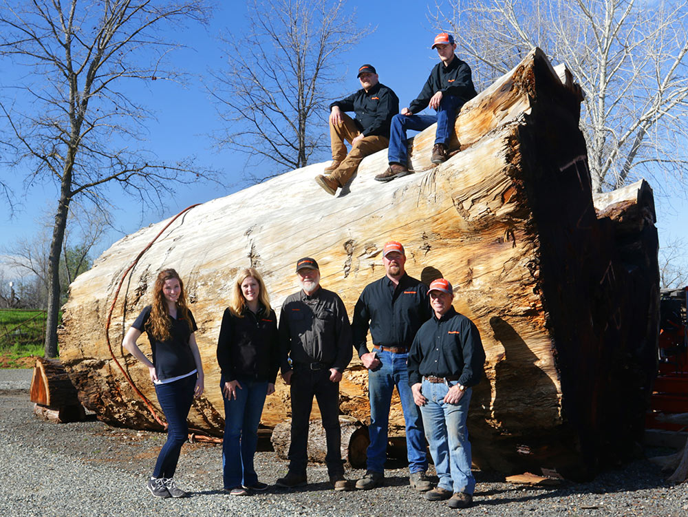 an image of the Far West staff standing in front of a very large tree trunk that is about 15 feet high, with 2 of the staff members sitting on top and 5 below on the ground level.