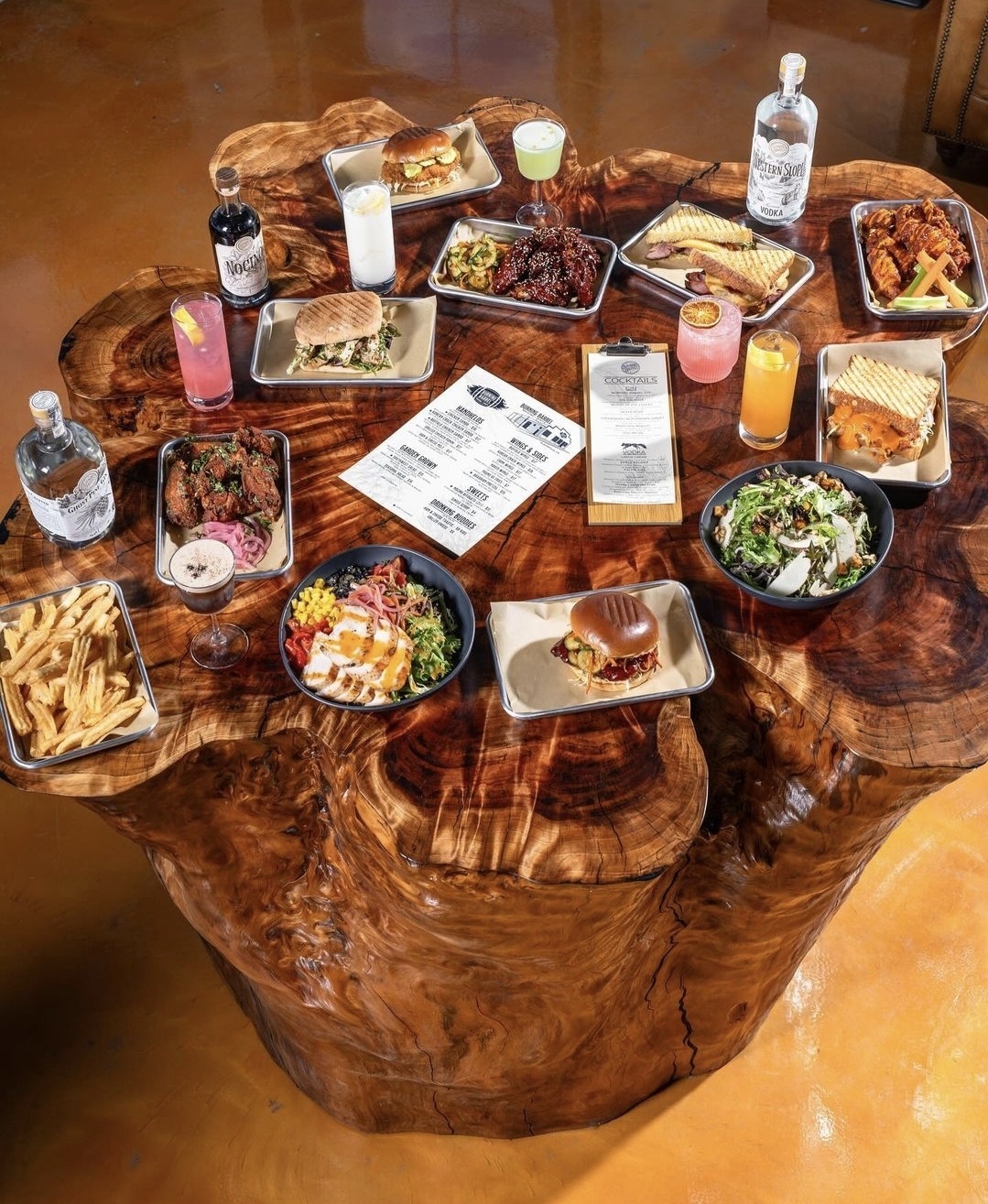 Chinese redwood bar height solid wood table base - with various brews, spirits, cocktails and food plates on it.